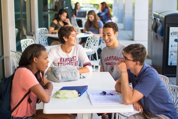 学生 engage in a discussion at a table area on campus.