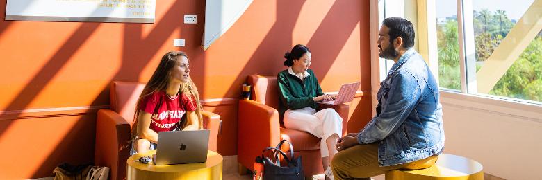 Three Chapman University students sit in lounge area on campus with their laptops